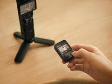 Load image into Gallery viewer, Hand holding a small remote screen controller with live preview and record button, controlling the DJI Osmo Pocket 4P on a mini tripod