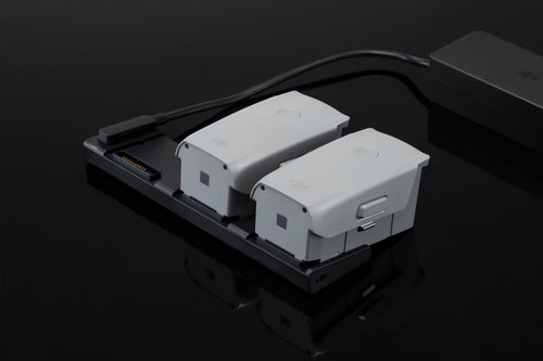 Two DJI Mavic Air 2 Drone Batteries Are Shown In A Charging Hub, Which Is Connected To A Power Adapter.