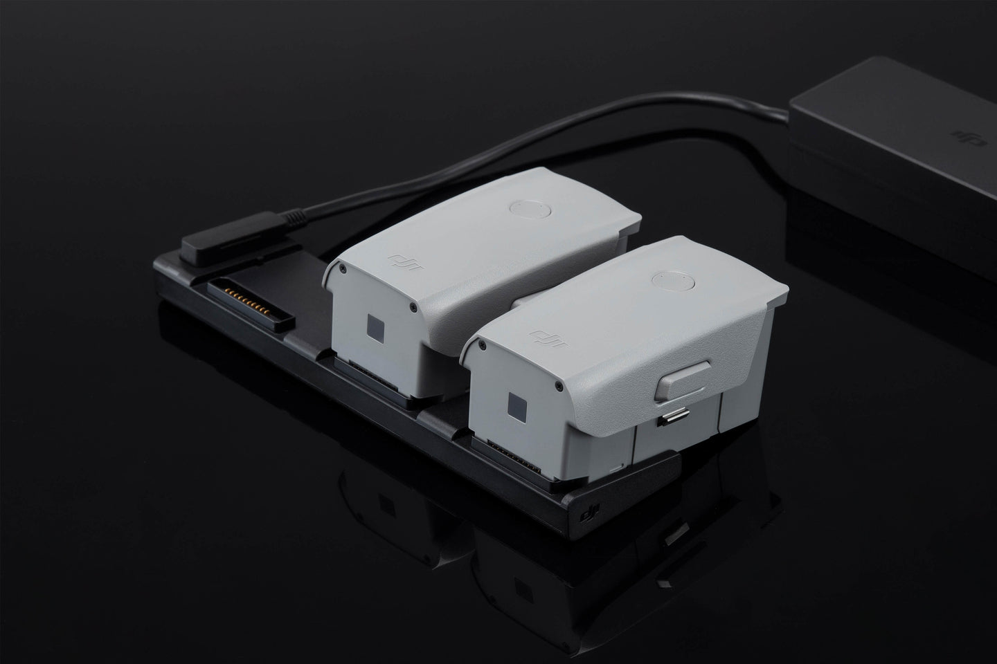Two DJI Mavic Air 2 Drone Batteries Are Shown In A Charging Hub, Which Is Connected To A Power Adapter.