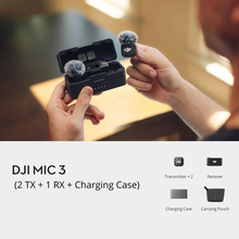 गैलरी व्यूवर में इमेज लोड करें, A person holds an open DJI DJI Mic 3 charging case with a small microphone attached, while another hand holds a matching transmitter. 
