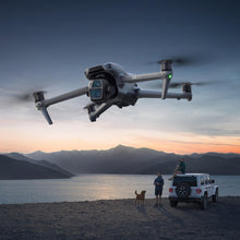 Load image into Gallery viewer, DJI Air 3S drone flying over a lake at sunset while a man with the controller stands beside an SUV
